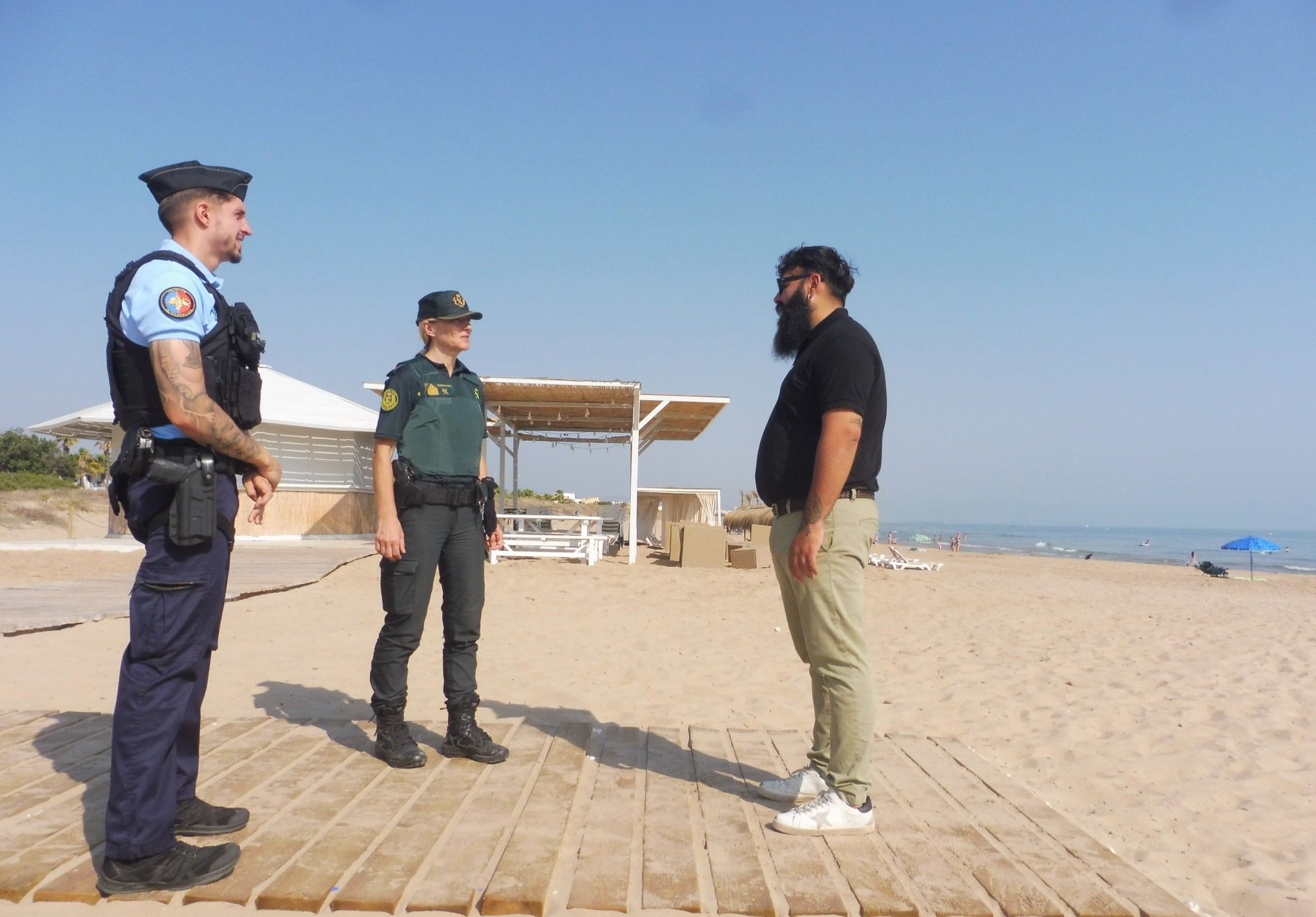 El gendarme francés y la sargento charlan con un empleado del Camping Kikopark en la playa de Oliva.