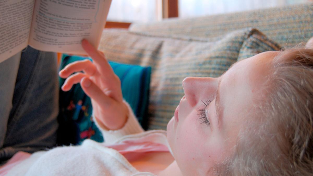 Unha rapaza le un libro tumbada no sofá.