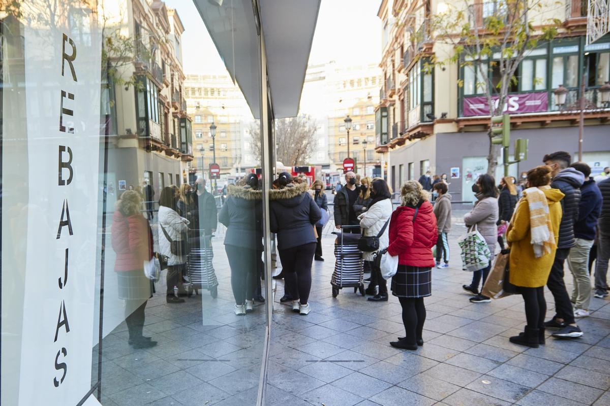 Detalle de un cartel de rebajas y varias personas esperando que abran los negocios durante el primer día de las rebajas, a 7 de enero de 2022 en Sevilla