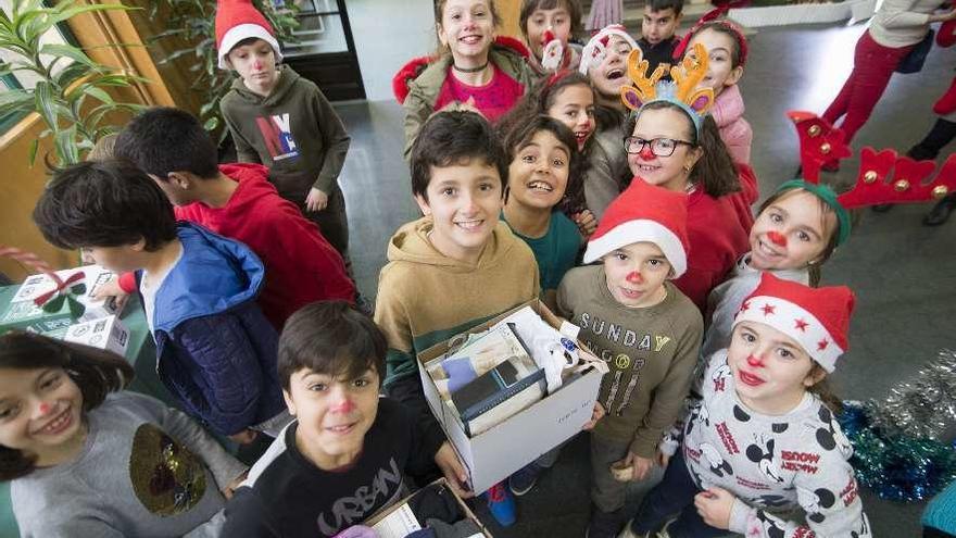 Alumnos del colegio Palacio Valdés, ayer, con la nariz pintada de rojo y adornos navideños en la cabeza , sostienen unas cajas con ropa interior que entregarán a Cáritas.
