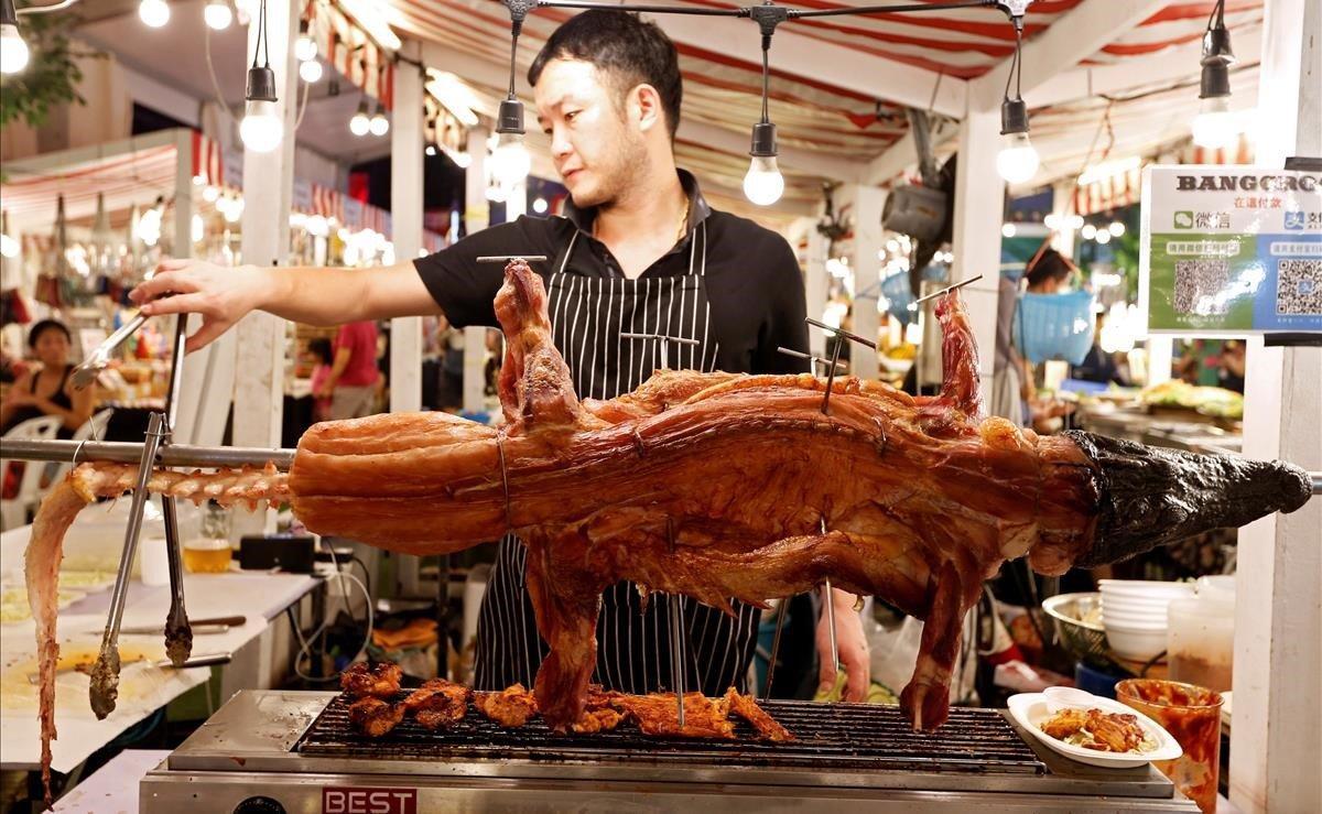 Un hombre cocina cocodrilo en una barbacoa en un mercado nocturno durante el año nuevo chino en Bangkok, Tailandia.