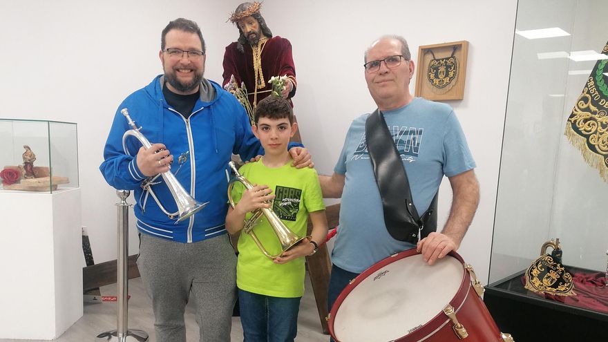 Los tres músicos miembros de una misa familia posan con sus instrumentos y la imagen titular de la Banda.