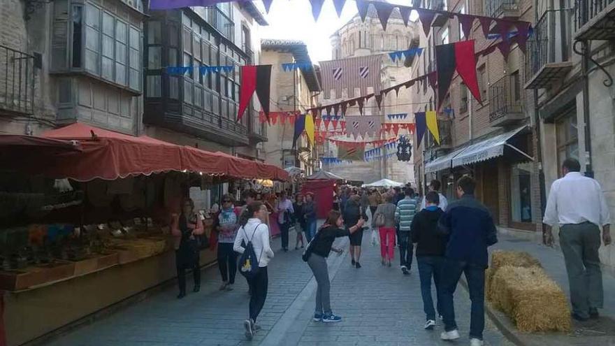 Toresanos y visitantes recorren los diferentes puestos instalados en el recorrido del Mercado Medieval con La Colegiata al fondo. Foro