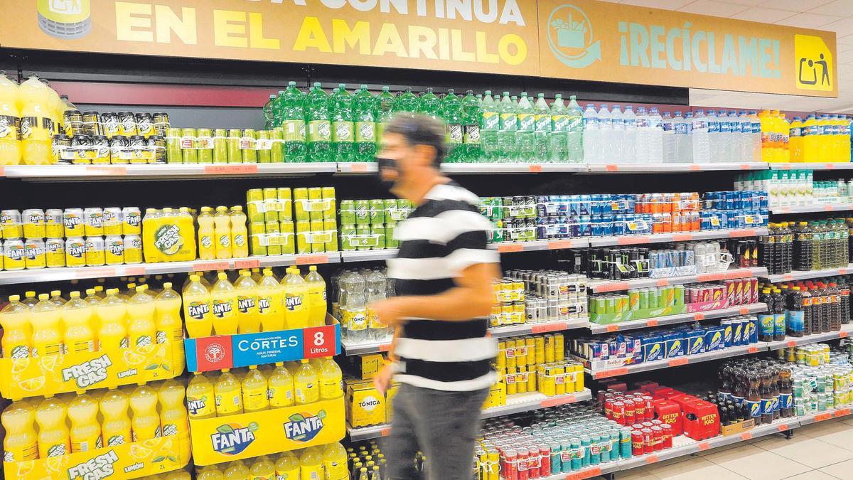 Un cliente pasa por delante del lineal de refrescos, donde se observa un cartel que explica dónde depositar estos envases.