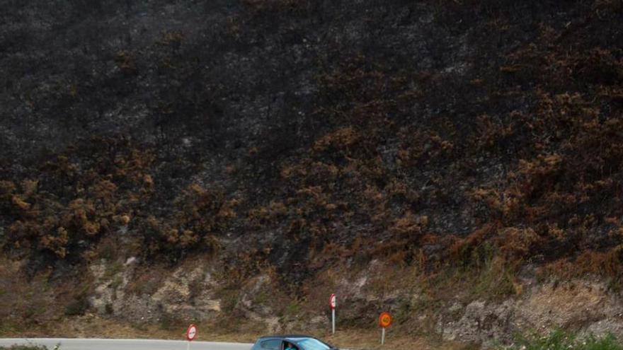 Un coche circula por la carretera cerca de donde el fuego arrasó la vegetación.