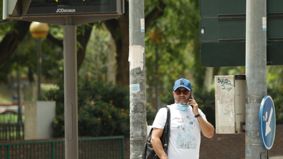 Un hombre hablando por teléfono bajo un termómetro que marca 44 °C en Valencia.