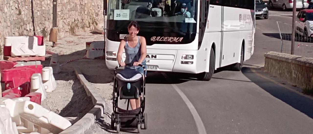 Una mujer, ayer, con un carrito de bebé por la carretera y detrás, un autobús de turistas.