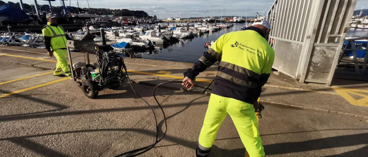 Operarios trabajando en el puerto de Bueu para marcar los espacios para depositar los aparejos y pertrechos de pesca.   | // SANTOS ÁLVAREZ