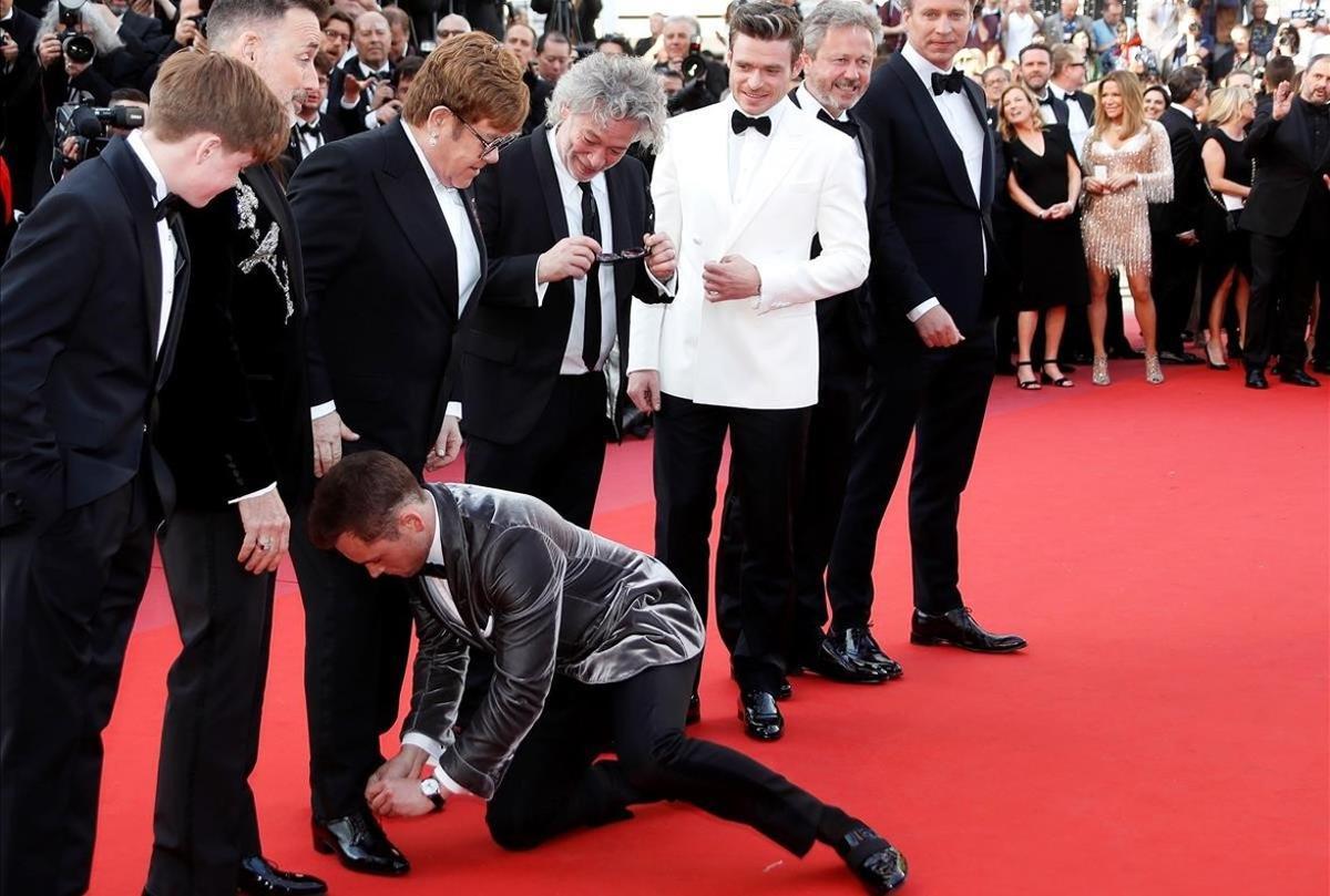 El actor británico Taron Egerton ata los cordones del cantante británico Elton John frente a la mirada del productor canadiense David Furnish, el cineasta y actor británico Dexter Fletcher; el actor británico Richard Madden y el productor británico Adam Bohling , durante su llegada al estreno de la película de Fletcher, Rocketman, este jueves durante la 72 edición del Festival de Cannes (Francia).