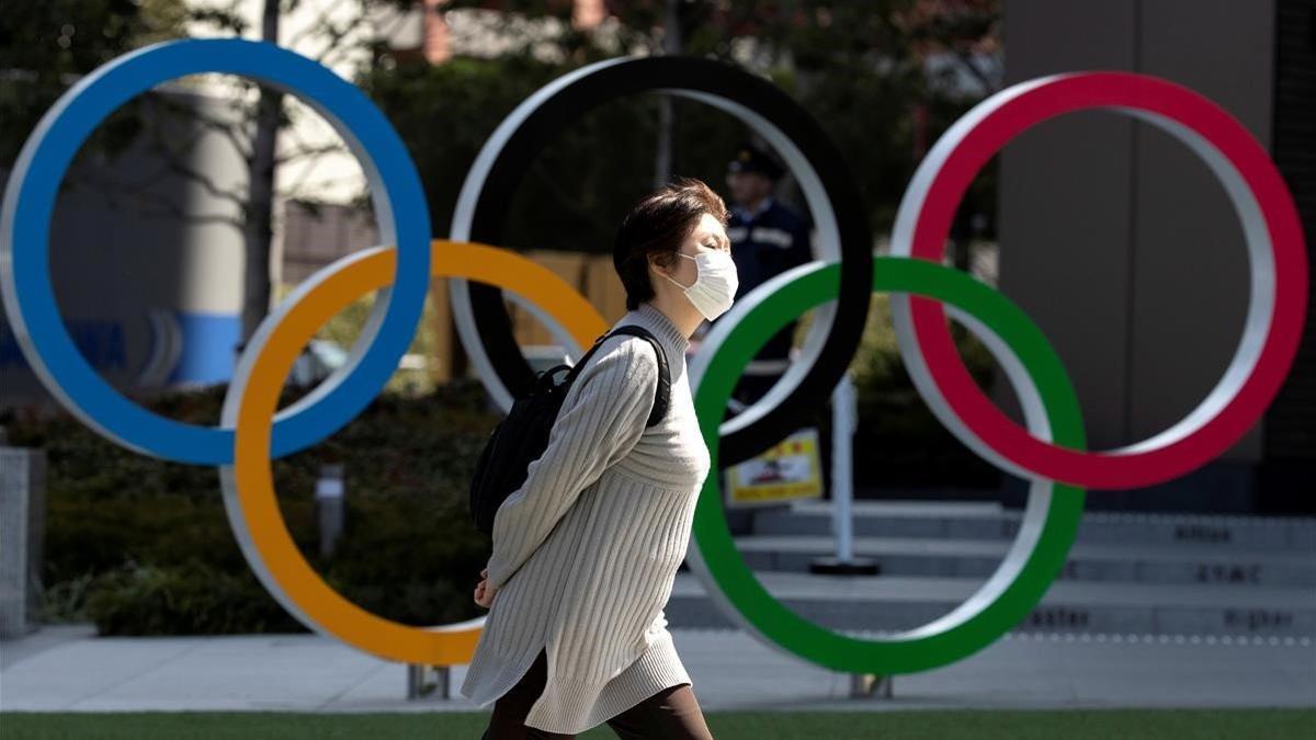 Una mujer con una máscara pasa frente a un símbolo olímpico en Tokio.