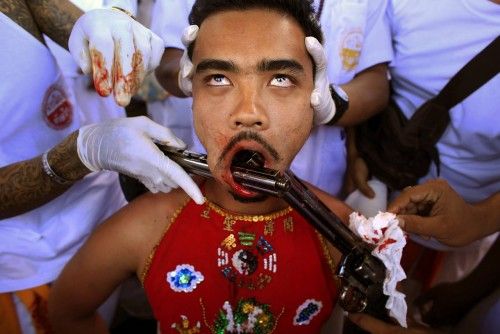 A devotee of the Chinese Bang Neow Shrine has two guns pierced through his cheeks before the beginning of a street procession during the annual vegetarian festival in Phuket