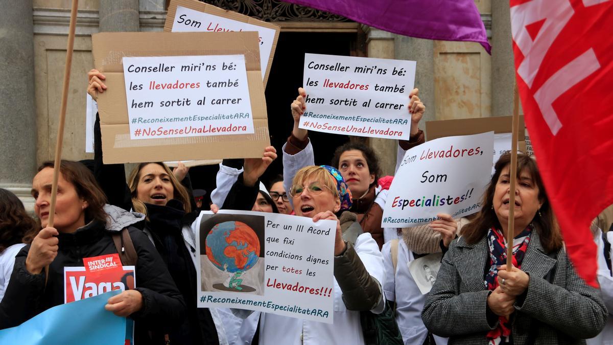 Llevadores en una concentració a la plaça de Sant Jaume de Barcelona porten cartells en què reivindiquen &quot;condicions dignes&quot; i remarquen que són &quot;especialistes&quot;, en la primera jornada de vaga convocada per la Intersindical al sistema sanitari.