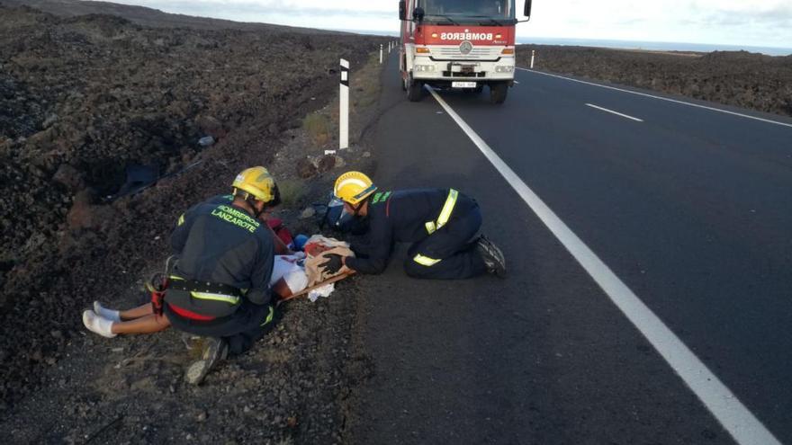 Dos bomberos del Consorcio de Emergencias asisten, hoy, a la mujer accidentada en la carretera entre Yaiza y Playa Blanca.