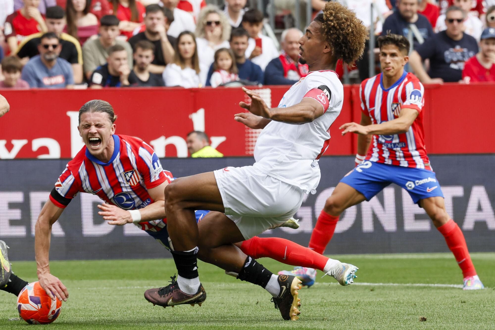 SEVILLA, 06/04/2025.- El centrocampista inglés del Atlético de Madrid Conor Gallagher (izda) recibe la falta del defensa francés del Sevilla FC Loic Badé, durante el partido de LaLiga que disputan este domingo en el estadio Ramón Sánchez-Pizjuán. EFE/José Manuel Vidal