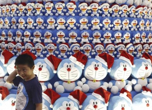 Un niño japonés con una camiseta Doraemon posa junto a un árbol de navidad hecho de muñecos de Doraemon, en un centro comercial de Singapur, 24 de noviembre de 2014.