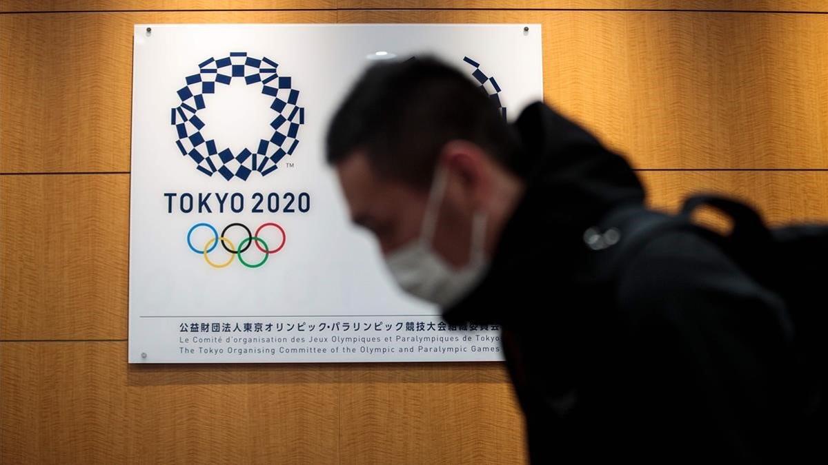 Un hombre con mascarilla pasa junto a un logo de los Juegos Olímpicos de Tokio, en la sede de la organización, en la capital japonesa.