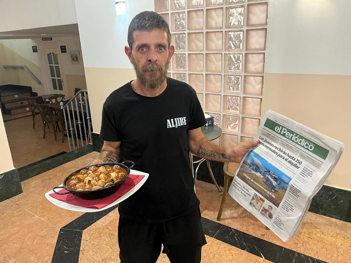 José Ortega sostiene en una mano la tapa de caracoles y en la otra un ejemplar de El Periódico Extremadura.