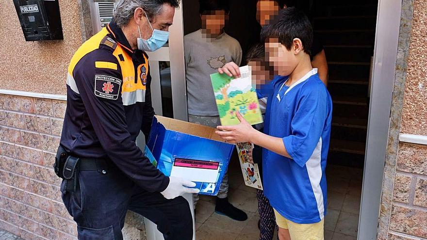 Un voluntario de Protección Civil de Aspe entregando ayer las tareas escolares a varios niños en un edificio.