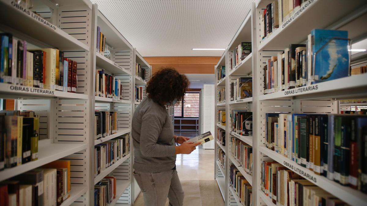 Una vecina trata de buscar un libro en una de las secciones de la biblioteca La Normal, con falta de iluminación.