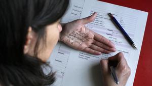 Una chica estudia matemáticas con una chuleta de fórmulas en su mano.