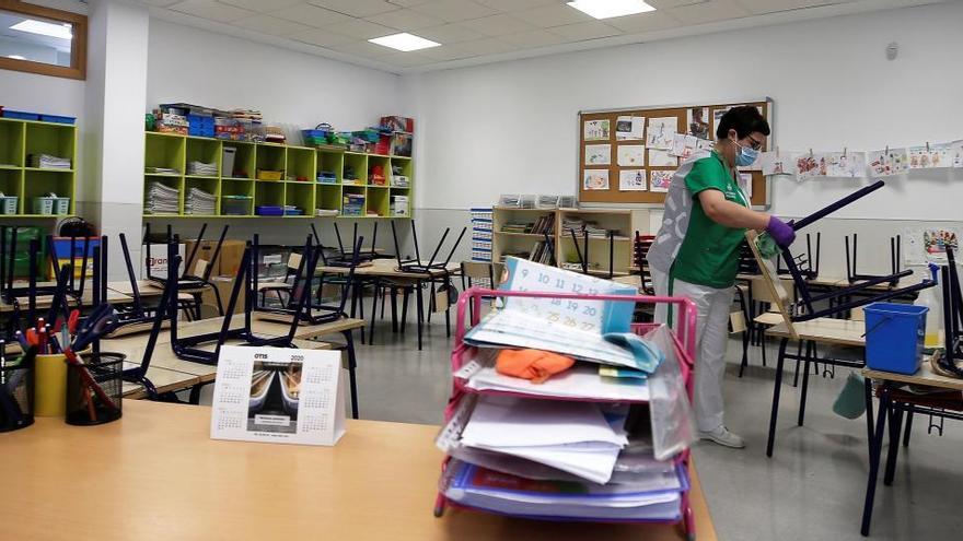 Una trabajadora del servicio de limpieza desinfecta las sillas y los pupitres de una clase de infantil.