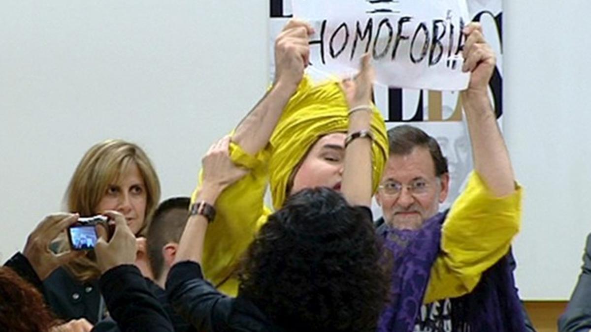 El 'drag queen' Shangay Lilly muestra una pancarta en la que califica de homófobo al PP ante la presencia de Mariano Rajoy, hoy en Madrid.