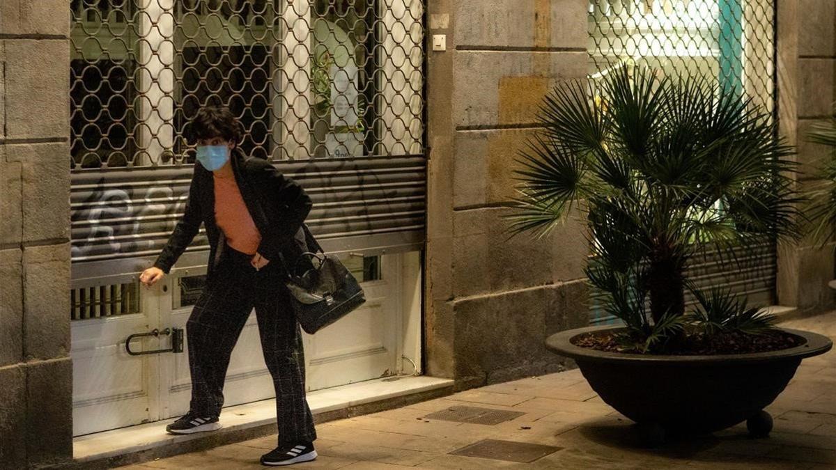 Una mujer con mascarilla echa el cierre a su negocio en Barcelona el 27 de octubre del 2020