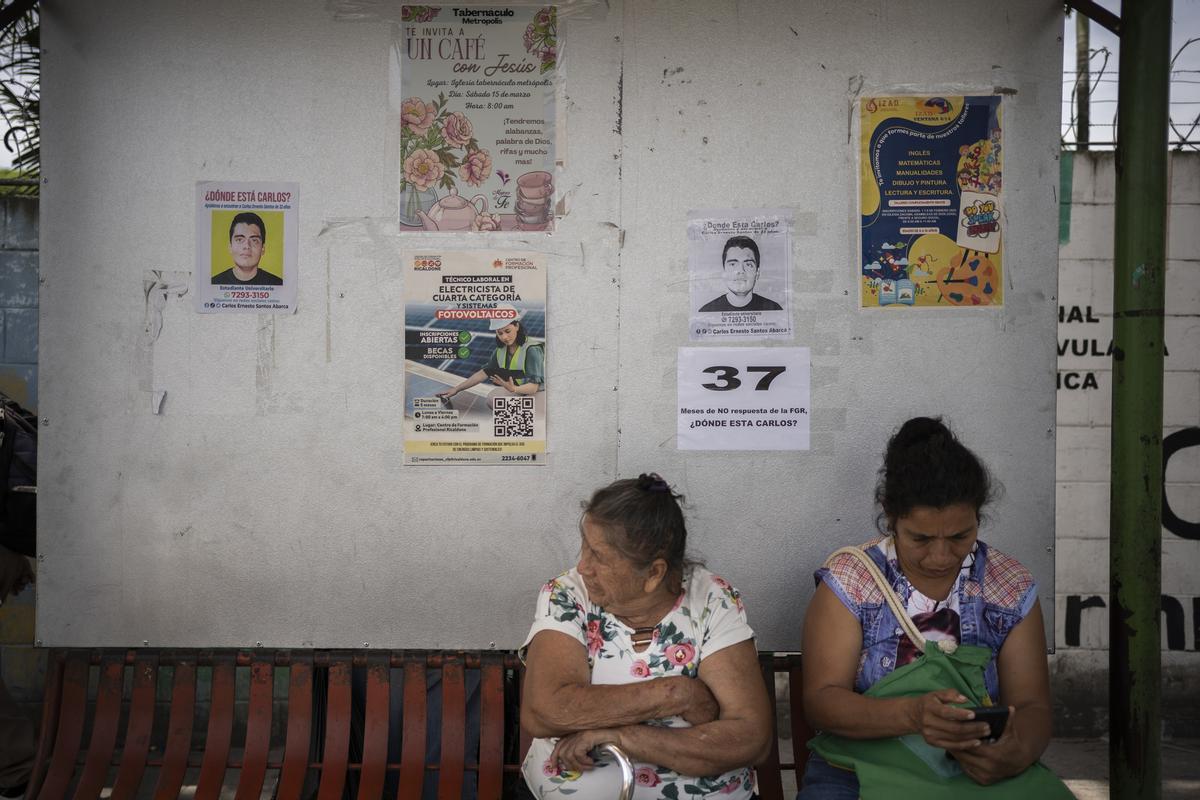 Dos mujeres en una parada de atobús junto a una foto de un joven desaparecido.