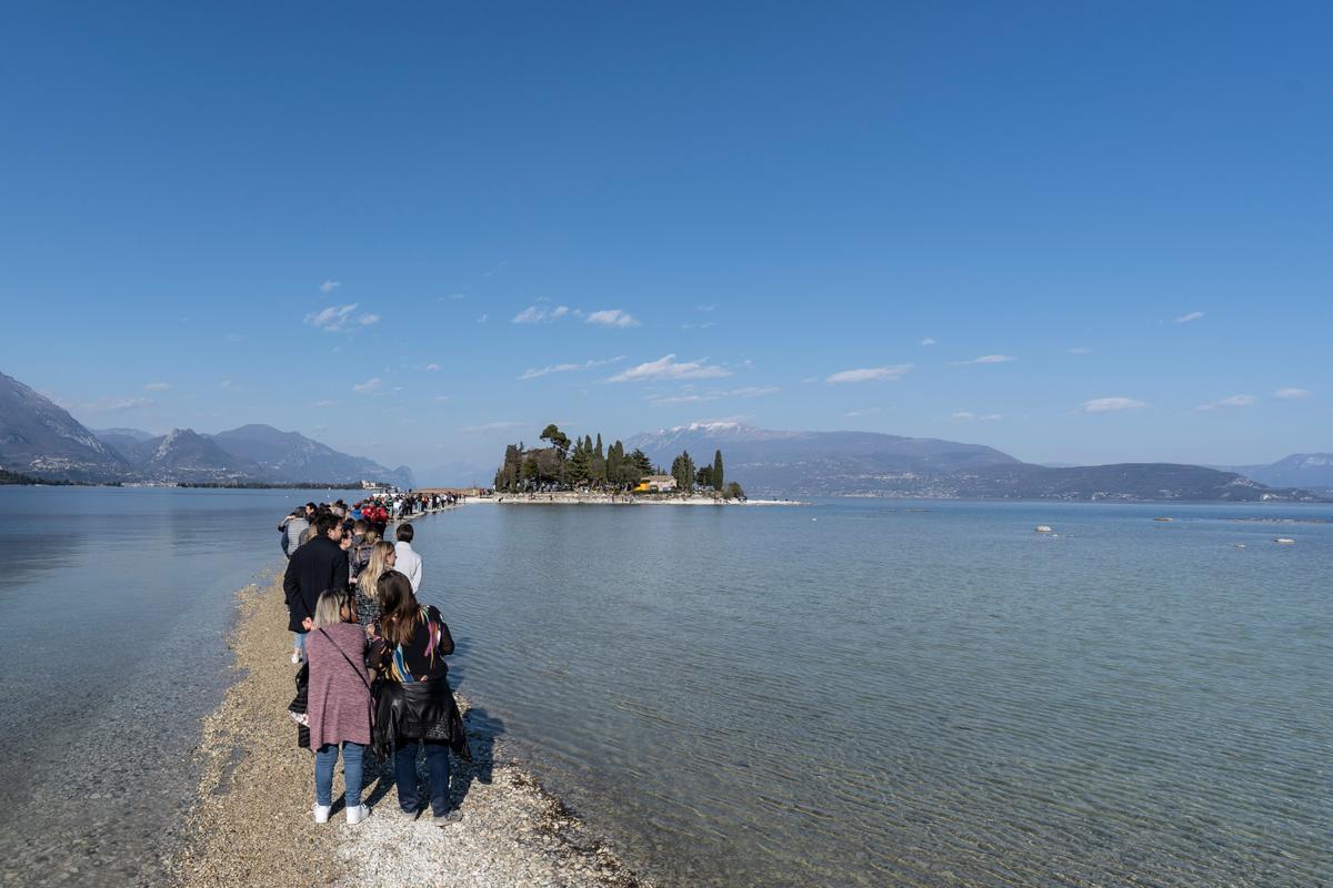 Italien, Gardasee: Menschen spazieren von Punta Belvedere nach Isola dei Conigli über den Gardasee aufgrund des ungewöhnlich niedrigen Wasserstands.