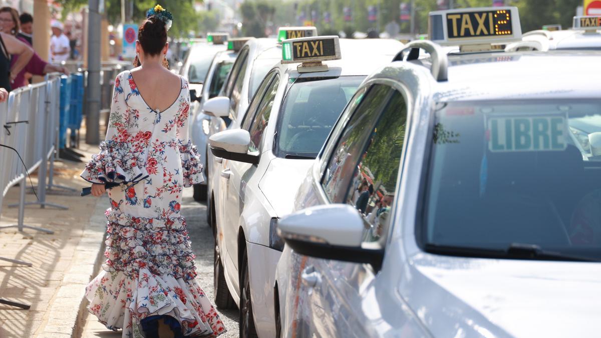 Una mujer vestida de flamenca camina por la hilera de taxis de una parada de la Feria de Abril de Sevilla.