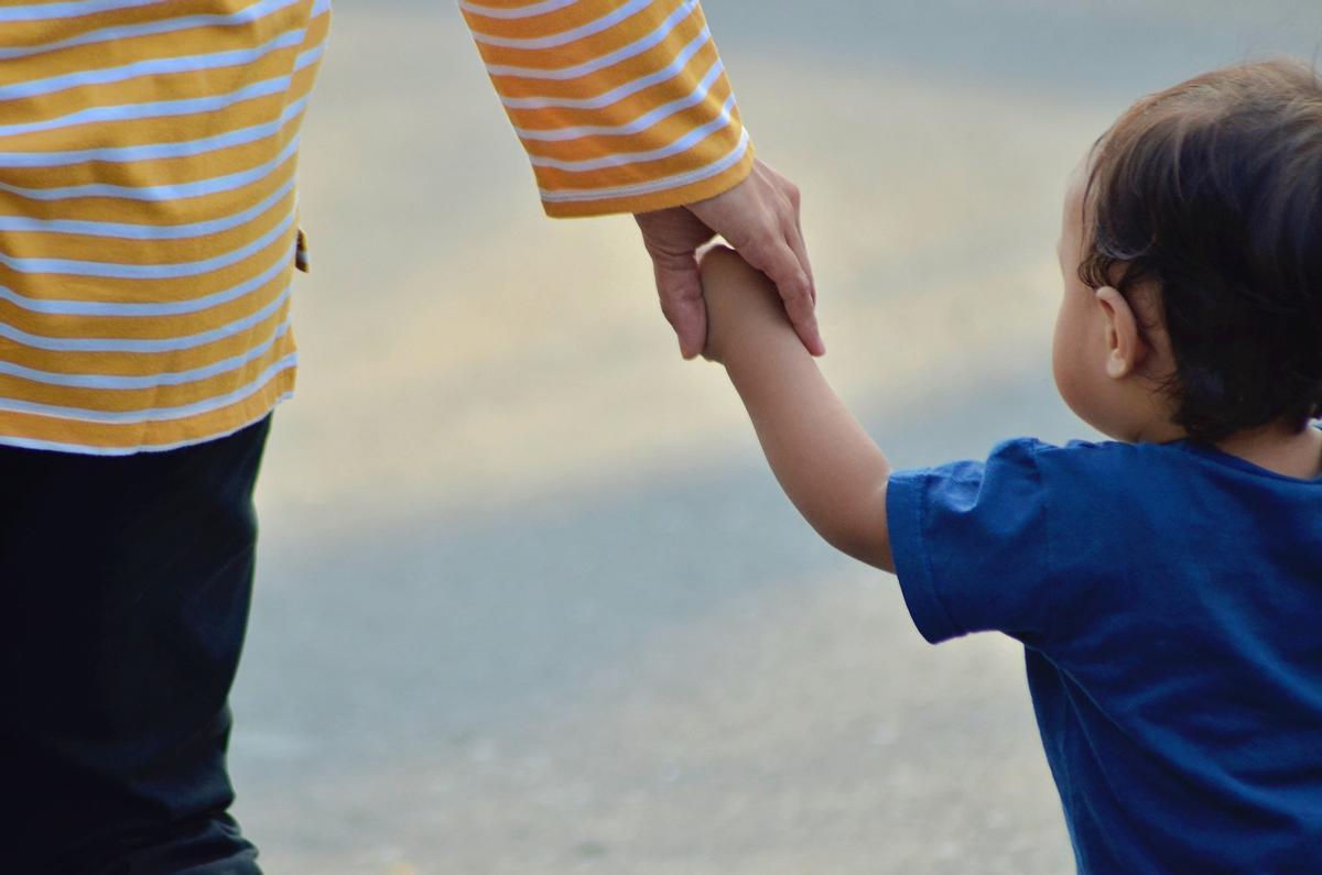 Una madre paseando con su hijo de la mano.