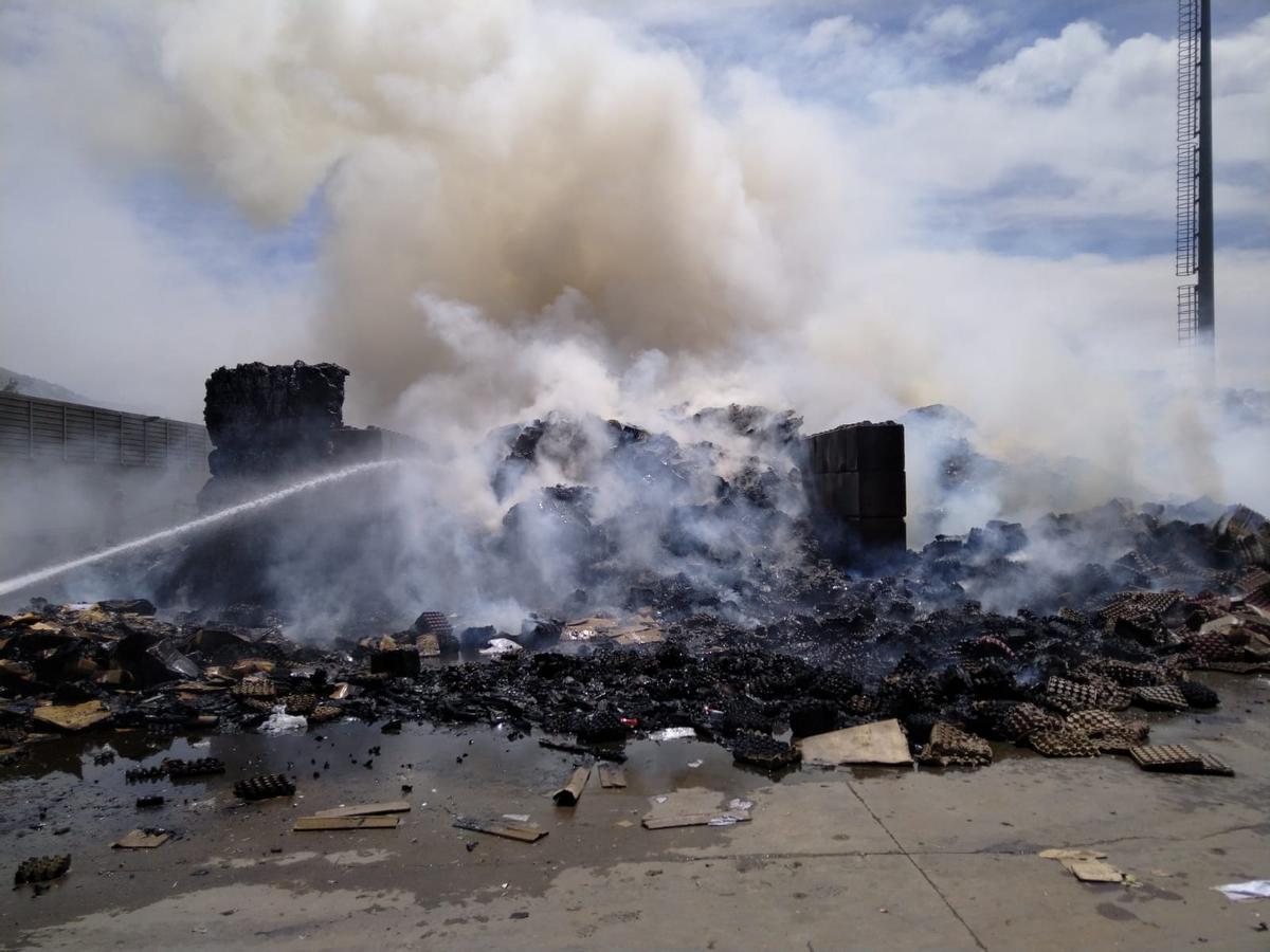 Un miembro del equipo antiincendios refresca un montón de residuos para evitar que se reaviven las llamas.