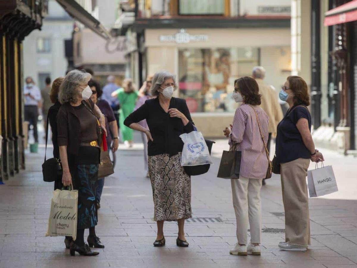 Varias personas con mascarillas conversan en una calle.