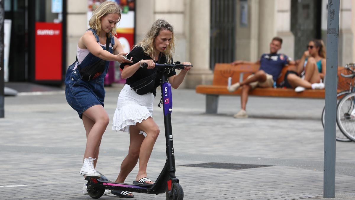 Dos jóvenes intentan subirse a un patinete compartido en Barcelona, en agosto de 2019, cuando las empresas operaban sin paraguas legal