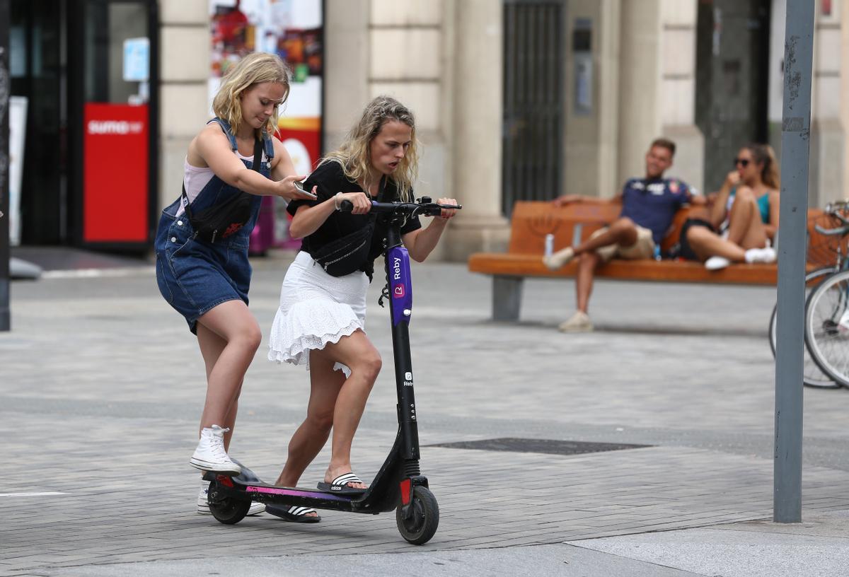 Dos jóvenes intentan subirse a un patinete compartido en Barcelona, en agosto de 2019, cuando las empresas operaban sin paraguas legal