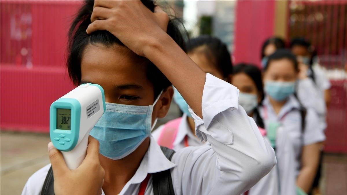 A los estudiantes con máscara facial se les toma la temperatura después de llegar al recinto escolar en Phnom Penh.