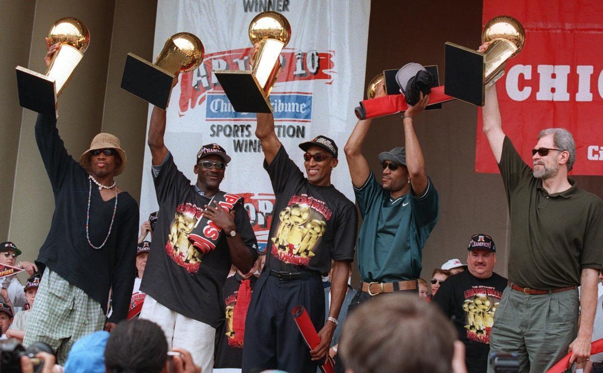 The Chicago Bulls' Dennis Rodman, left, Michael Jordan, Scottie Pippen, Ron Harper and coach Phil Jackson, right, hoist the team's five NBA Championship trophies aloft during a celebration in Chicago's Grant Park on Monday, June 16, 1997. The Bulls beat the Utah Jazz 4-2 in the best-of-7 NBA Finals. (AP Photo/Michael Conroy)