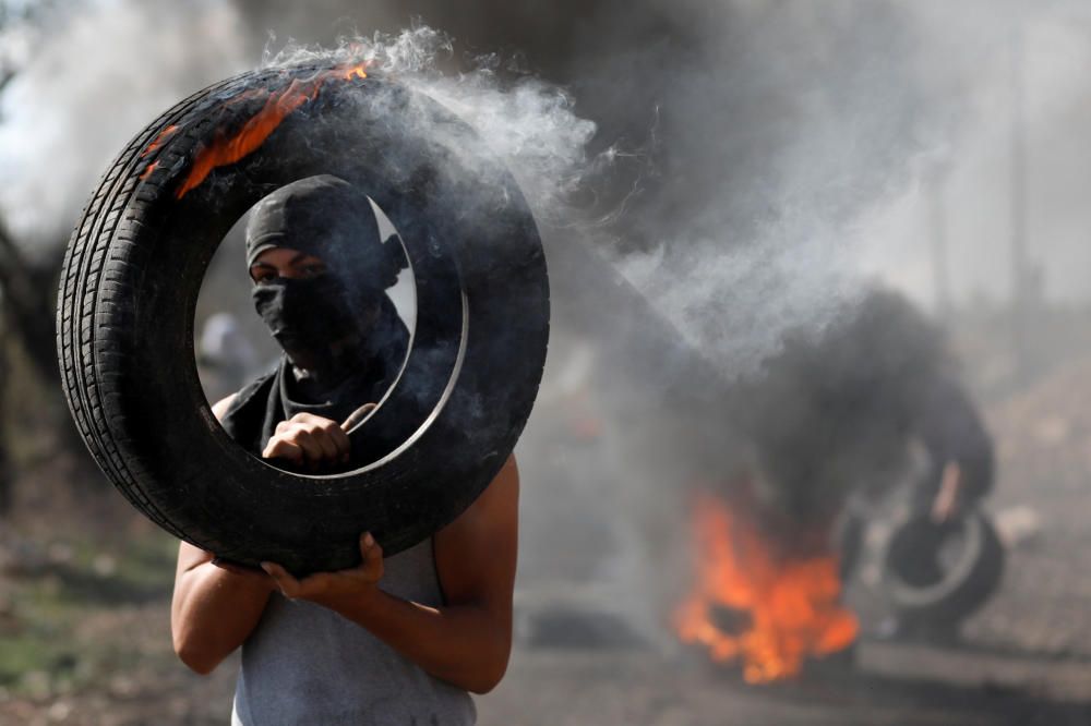 A Palestinian protester carries a burning tire ...