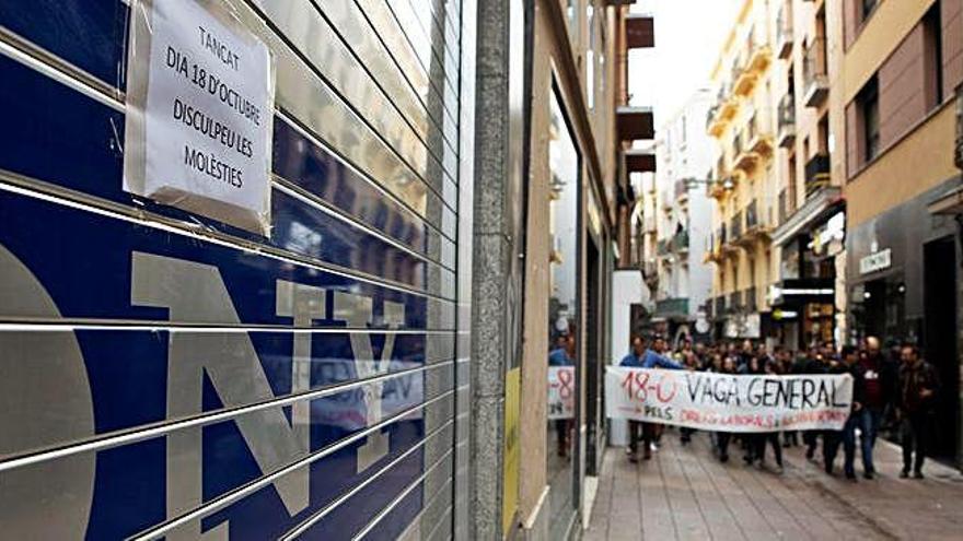 Un grup de manifestants caminen per un carrer de Lleida amb el comerç tancat
