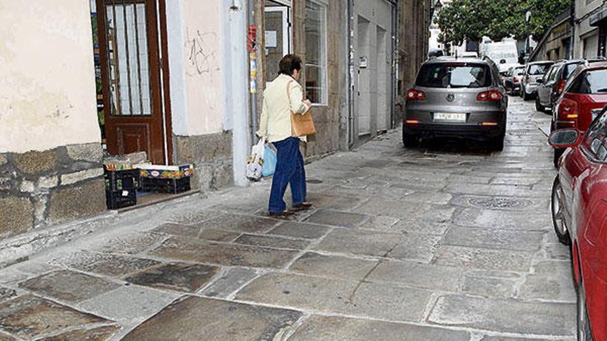 Una peatón camina por la Ciudad Vieja entre coches que circulan y que están aparcados. | thais r. paz