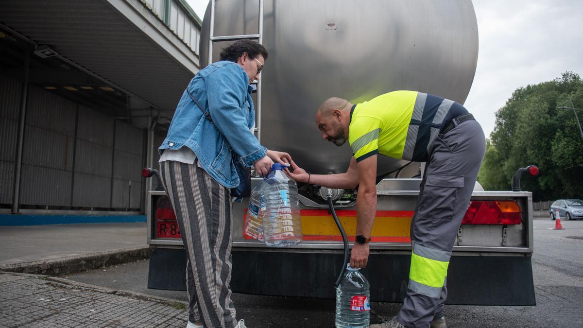 Una vecina de Betanzos llena unas garrafas con agua de una cisterna con la ayuda de un operario