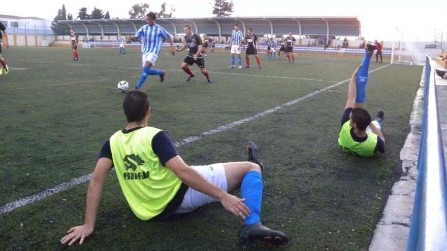 Dos futbolistas calientan en la banda, próximos al juego, en un partido de la Tercera División malagueña.