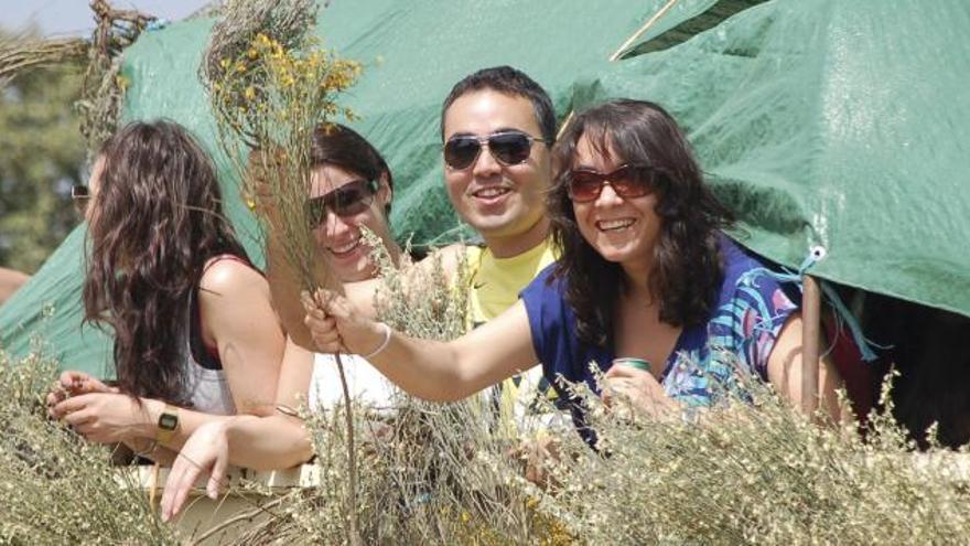 Un hombre atiende una paella y un grupo de romeros permanece bajo un árbol.