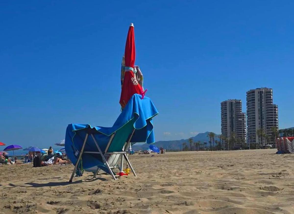 Una sombrilla y una silla solitarias, a mediodía, de bañistas que regresan después de comer a la playa.