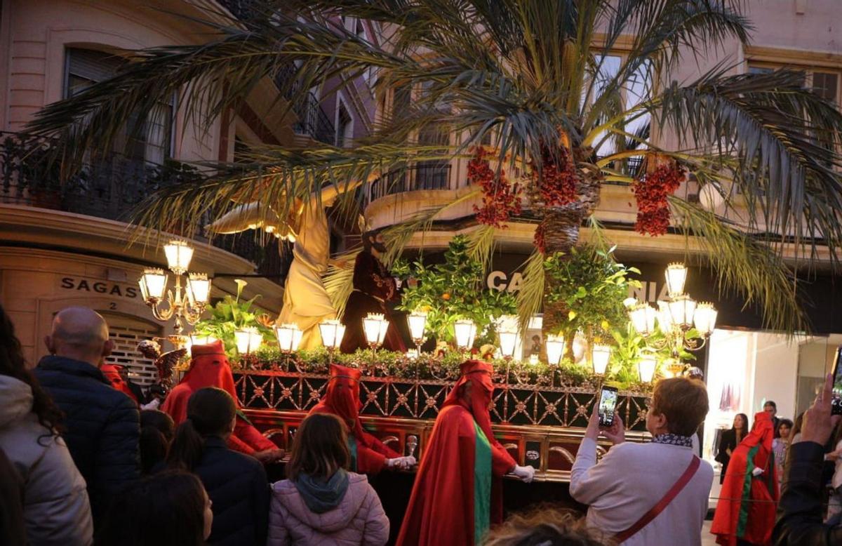 El espectacular trono de la Oración en el Huerto con una enorme palmera en el centro y árboles muy ilicitanos, y un grupo de jóvenes cofrades, que repartieron caramelos. | ANTONIO AMORÓS