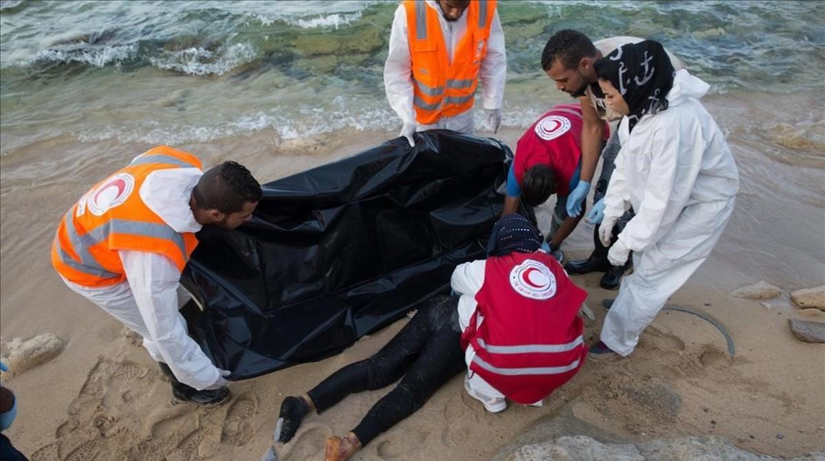 Miembros de la Media Luna Roja de Libia tratan de introducir en una bolsa el cadáver de un inmigrante ahogado y devuelto a la costa por las olas, en Trípoli (Libia), este sábado.