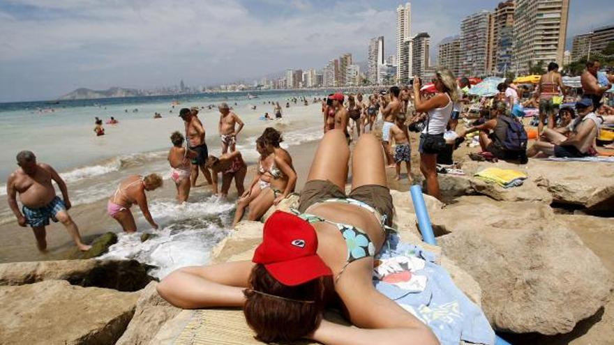 Una turista toma el sol sobre las rocas en la playa de Levante, en Benidorm.