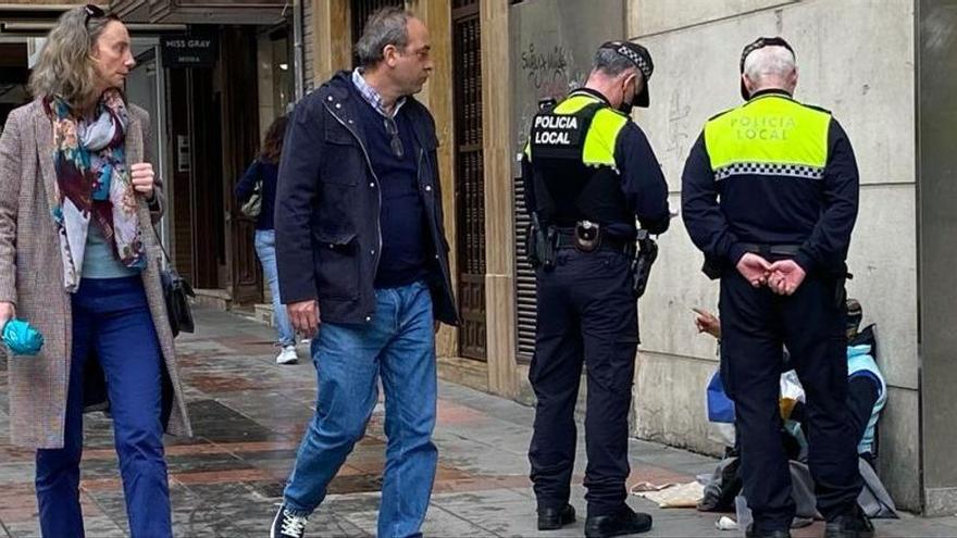 Dos viandantes observan a dos agentes de la Policía Local multando a una mujer sin recursos.