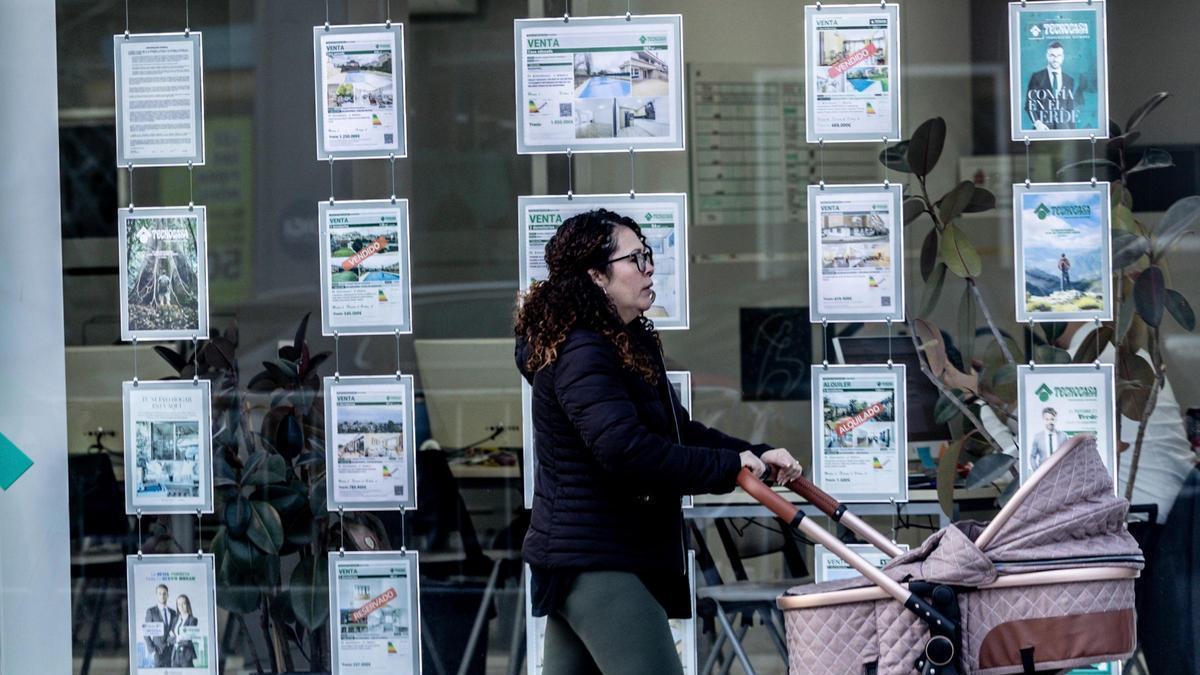 Una mujer pasa con un carrito de bebé junto a una inmobiliaria.