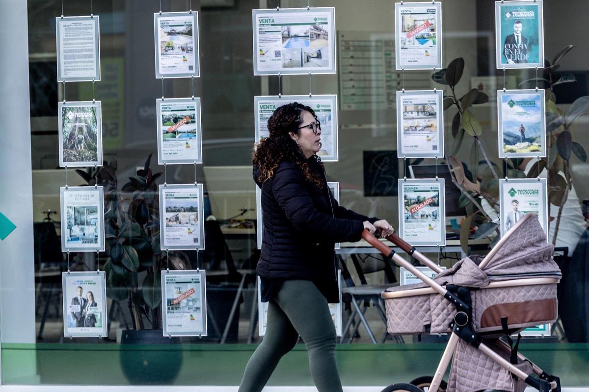 Una mujer pasa con un carrito de bebé junto a una inmobiliaria.